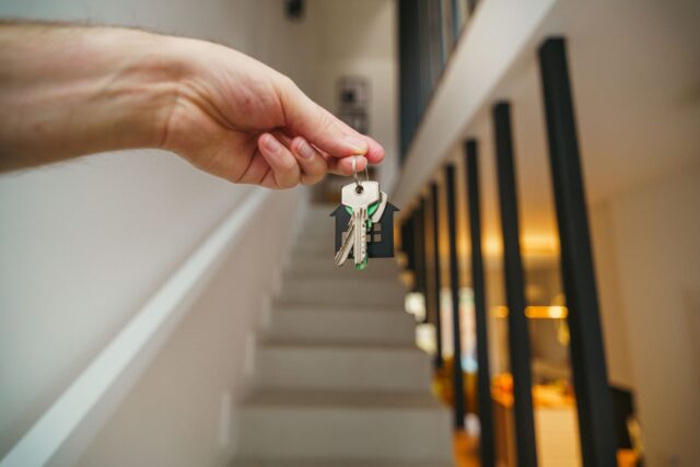 A hand holding house keys in a modern interior, symbolizing new home ownership or real estate investment. — plazos y consejos